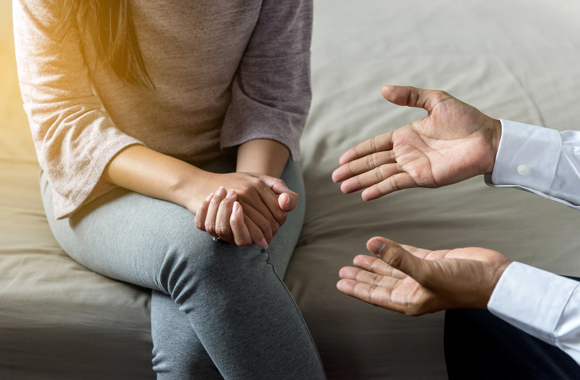 Das Motiv zeigt eine sitzende Frau und erklärende Hände eines Mannes