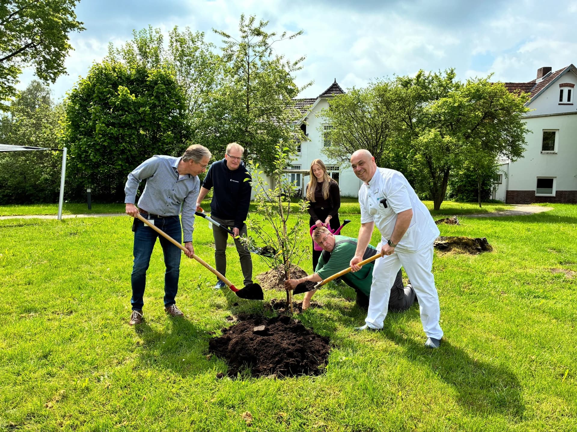 Mitglieder der Klinikleitung pflanzen einen Apfelbaum