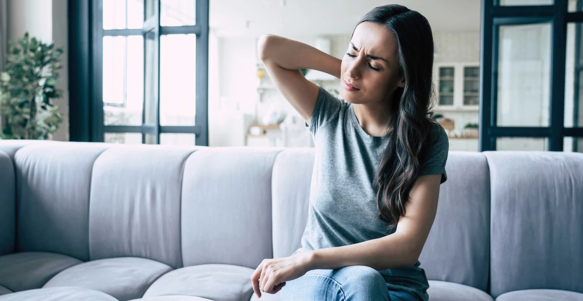 Das Motiv zeigt eine Frau auf einem Sofa, die sich an den Nacken fast