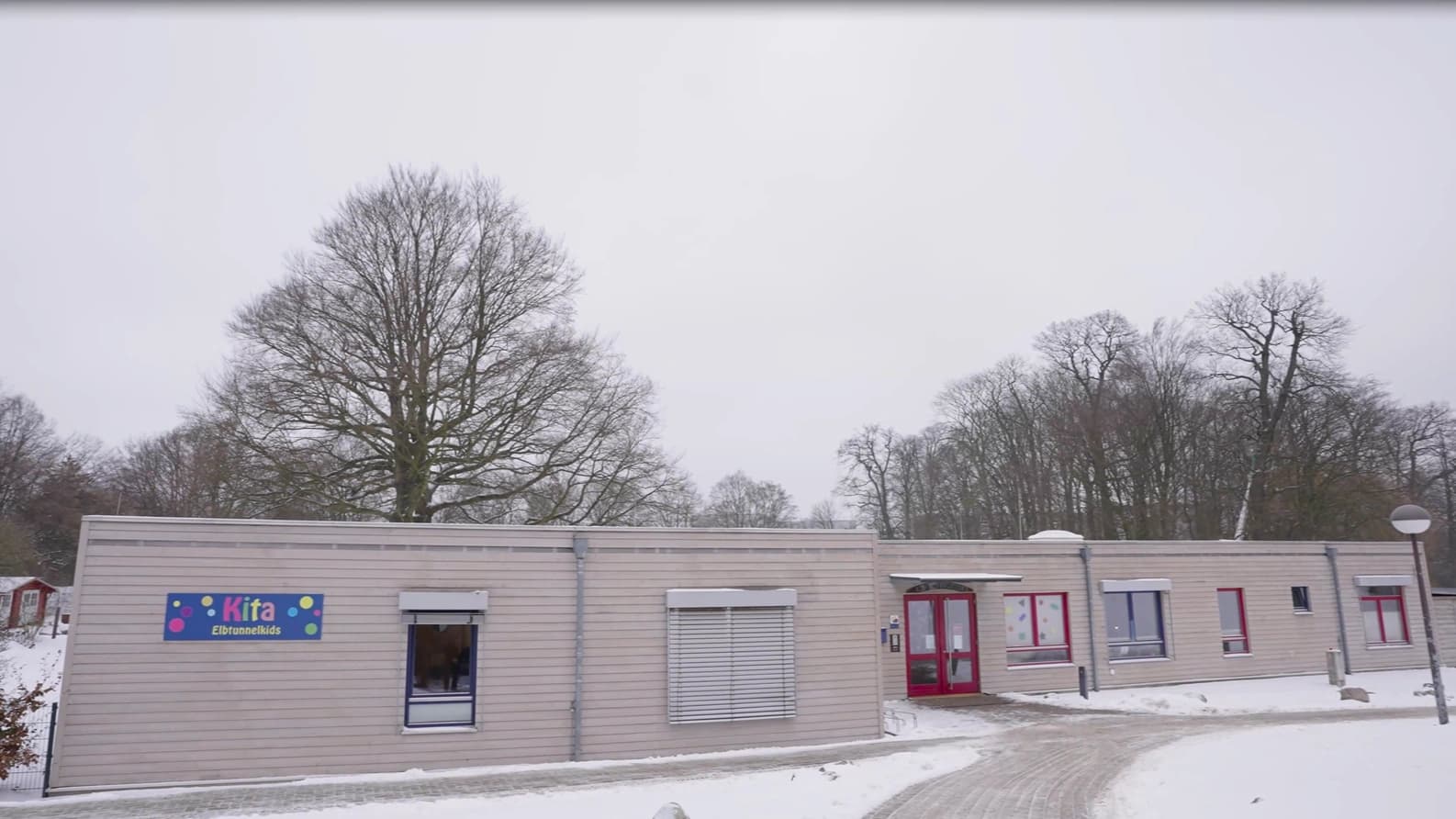 Bild: Holzgebäude der Kita im Schnee mit roten Fenstern