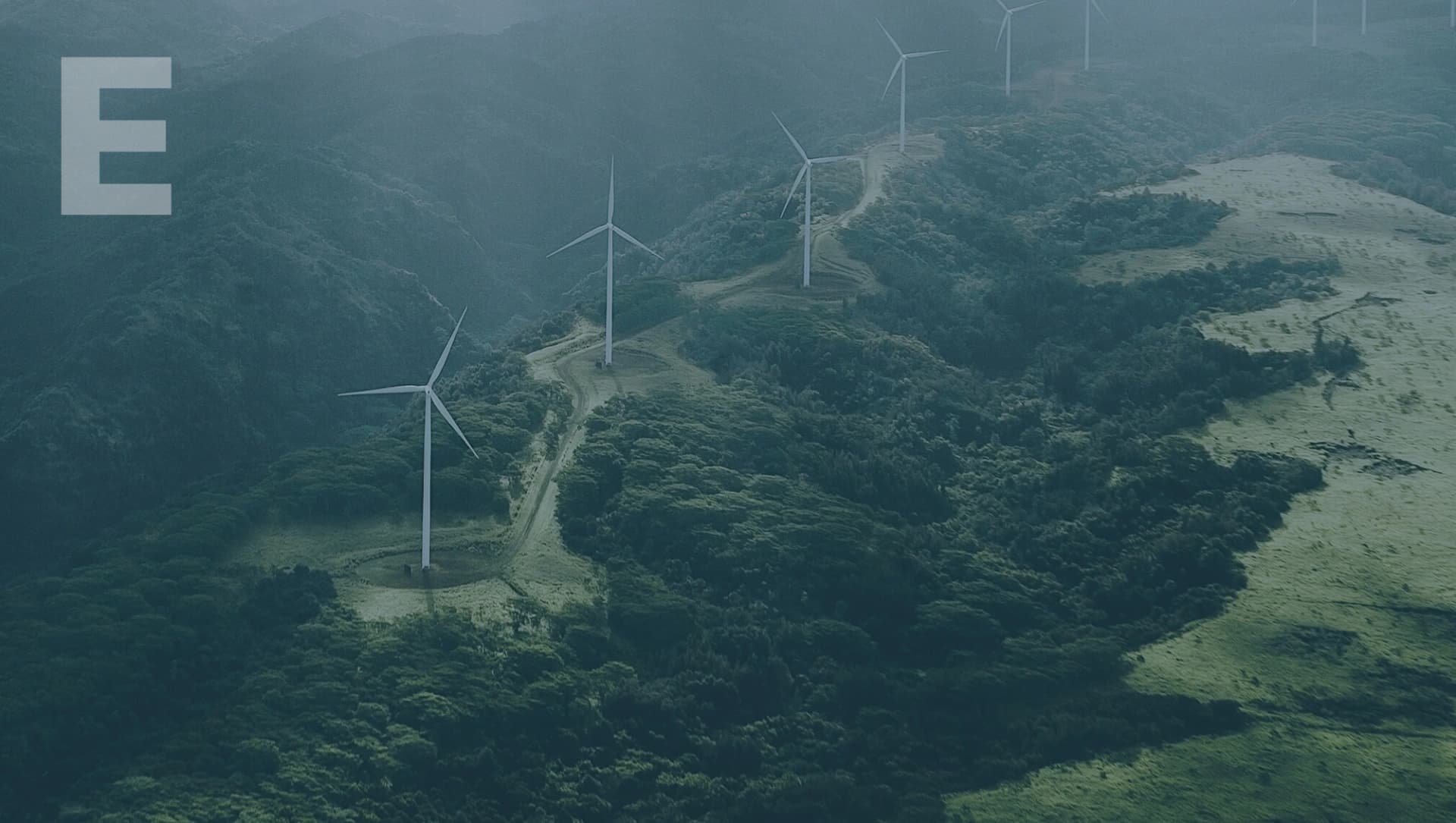 Landschaft mit mehreren Windkraftanlagen auf bewaldeten Hügeln unter bewölktem Himmel