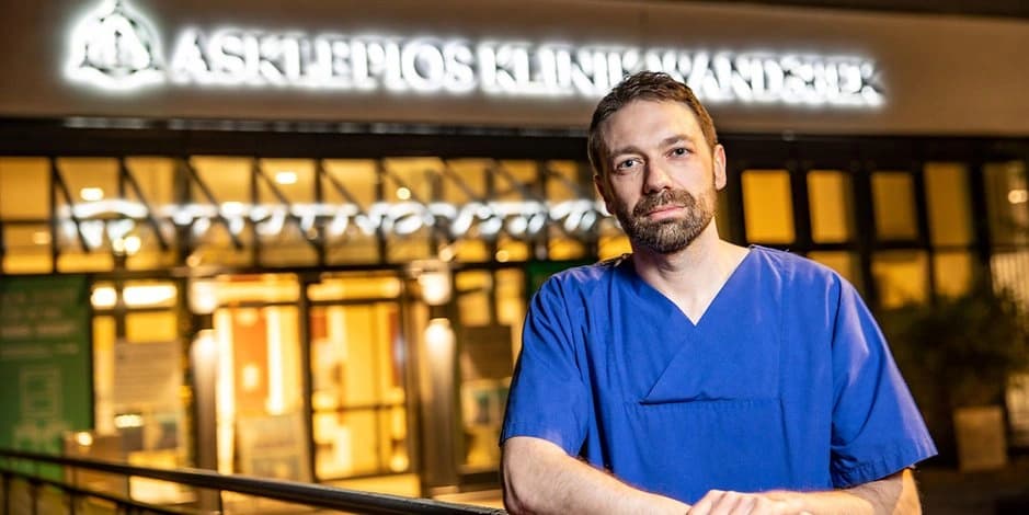 Text: Foto Lars Sigl am Abend vor der Asklepios Klinik Wandsbek im blauen Kassack lächelnd