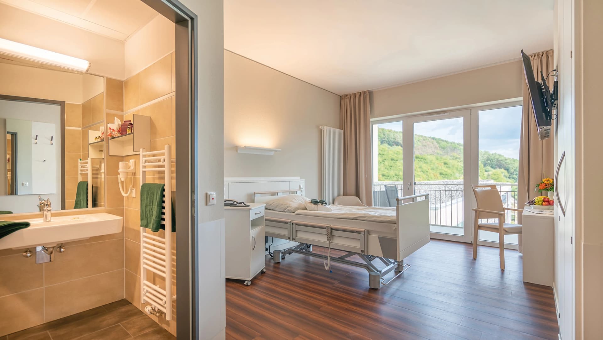 Patientenzimmer Neurologie mit Blick ins Bad und in das Zimmer mit Bett und Sitzbereich