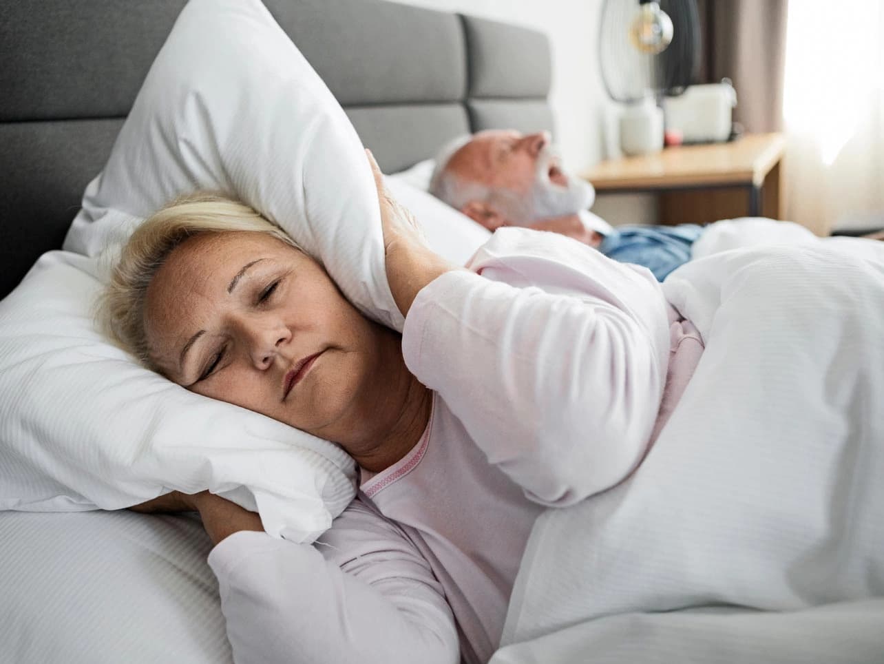 Bild: Frau im Bett hält sich die Ohren zu