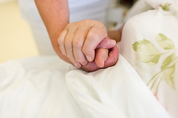 Zwei Menschen halten Hände Zuwendung am Patientenbett