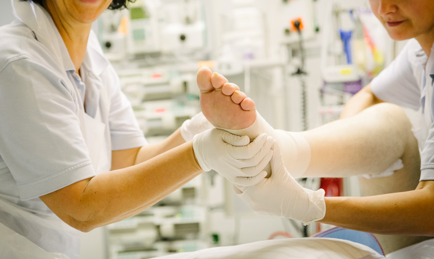 Beatmungszentrum Physiotherapie Bild: Pfleger hält den Fuß des Patienten für eine physiotherapeutische Übung