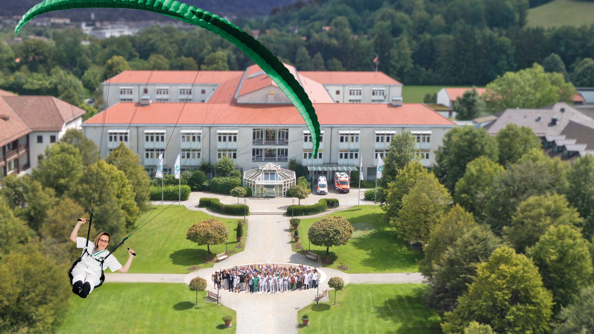 Foto: Gesundheits- und Krankenpflegerin mit Gleitschirm über der Asklepios Stadtklinik Bad Tölz